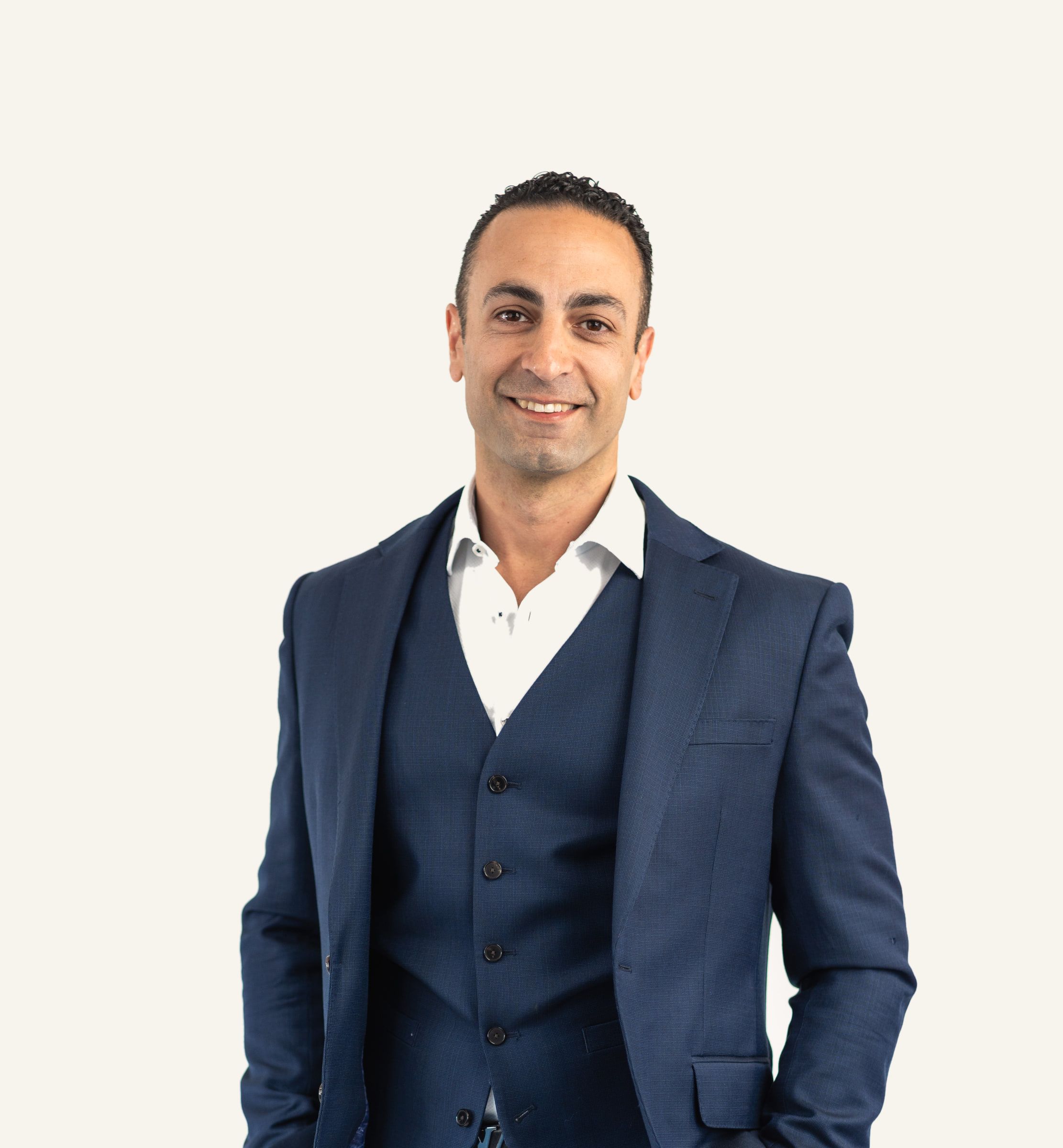 Mr Haider Jan, smiling, in a navy three-piece suit and open-collared shirt, with his hands in his pockets.